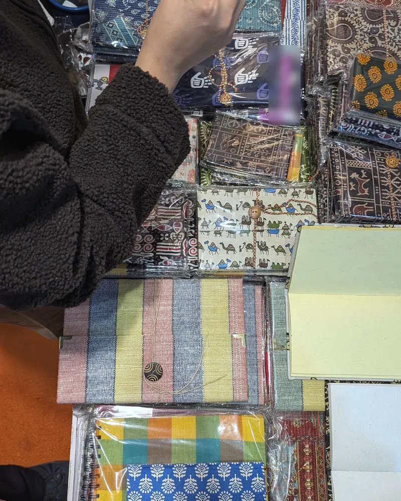 A visitor sorting through packs of printed textile products and fabric-covered notebooks on a table.