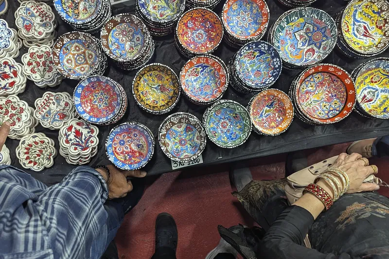 Hands reaching across a stand table covered with hand-painted ceramic bowls in bright patterns.