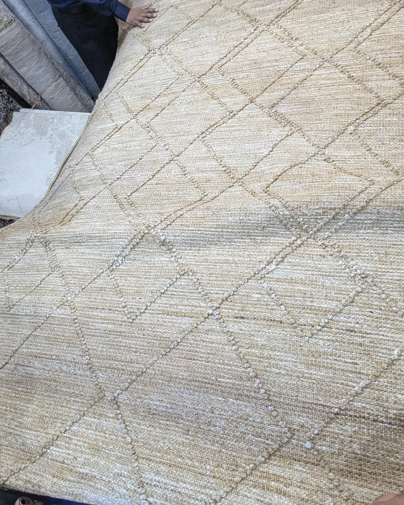 A natural-fibre rug with a diamond pattern held up to show its surface and weave.