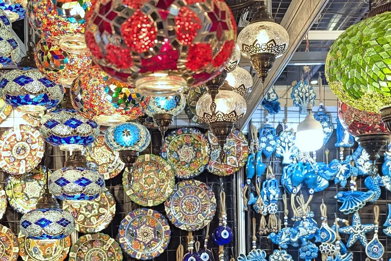 Mosaic glass lamps, painted plates and blue ceramic hangings crowding a stand wall.