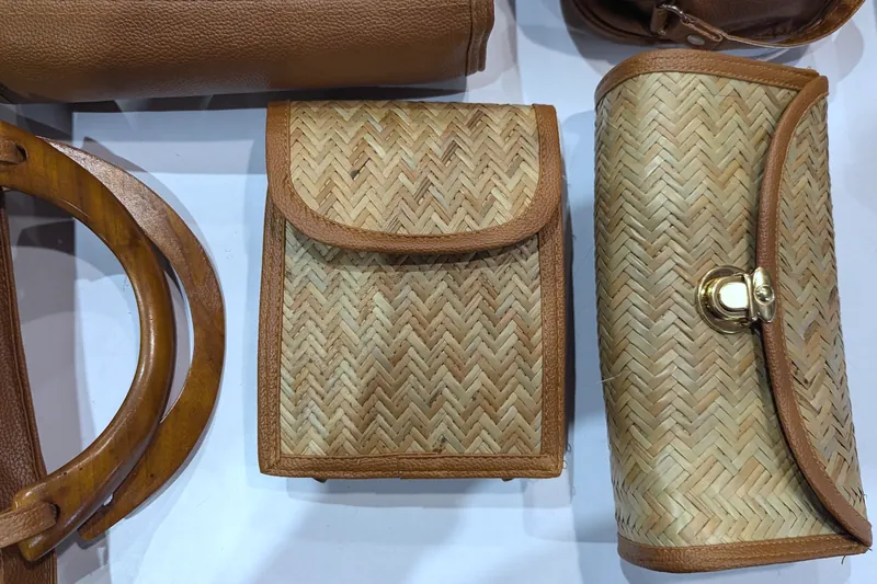 Two woven cane bags with tan leather trim laid side by side on a white table.