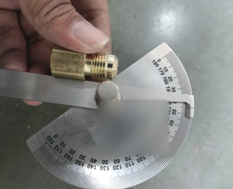A brass flare fitting held against a steel protractor to check the flare angle.