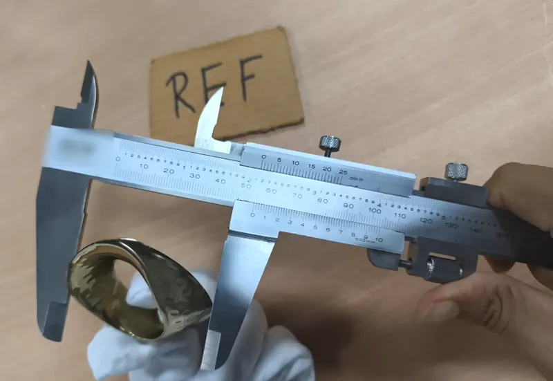 A hammered brass napkin ring held in a gloved hand and measured with a vernier caliper.