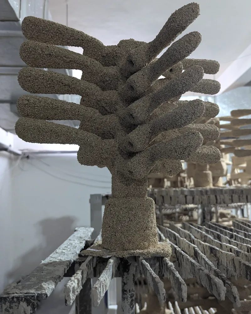 A wax tree coated in coarse ceramic stucco, standing on a drying rack among other shelled trees.
