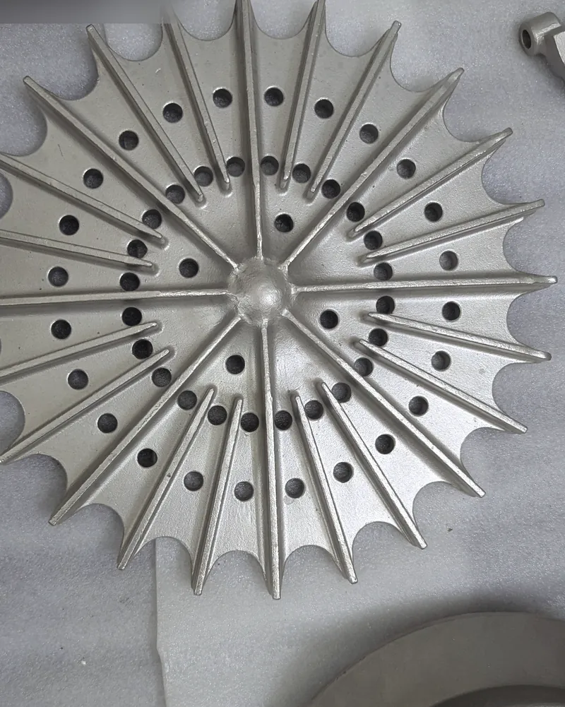 A large star-shaped stainless steel casting with radiating ribs and drilled holes, laid on a grey sheet.