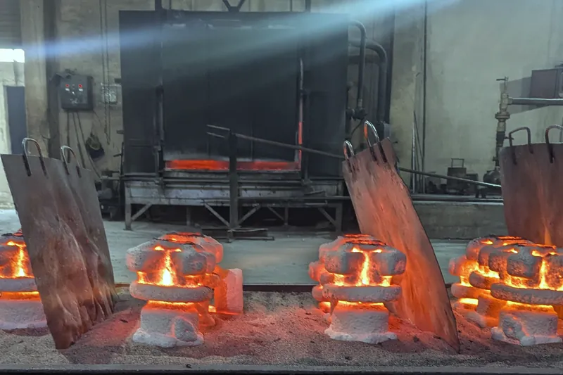 Glowing orange ceramic moulds on the floor in front of an open furnace, with steel shields leaning beside them.