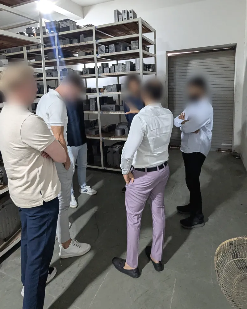 Visitors standing in front of labelled steel racks holding injection dies and tooling blocks; faces blurred.